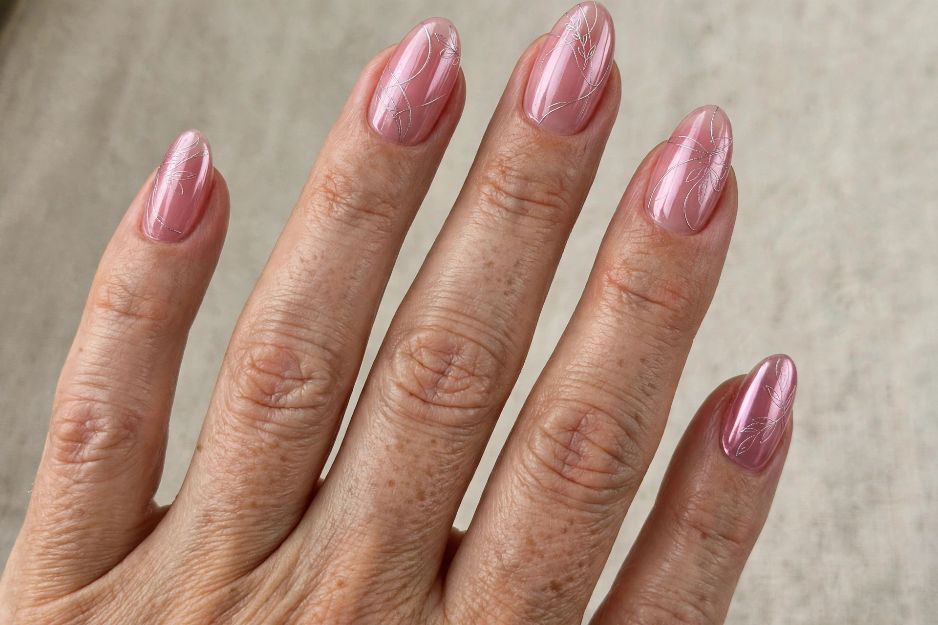 Jelly pink chrome nails with silver line art on almond nails